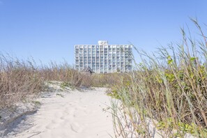 A sandy path leading to a modern building with multiple floors and large windows.