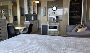 A hotel room with a bed, a dining table with chairs, a kitchenette, and a seating area with a sofa.
