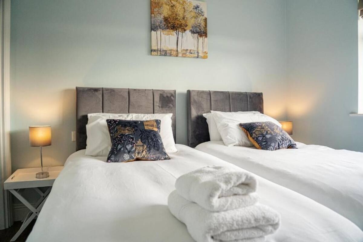 Ein Doppelbett mit weißen Laken, zwei Kissen, ein gefaltetes Handtuch und ein Nachttisch mit Lampe.