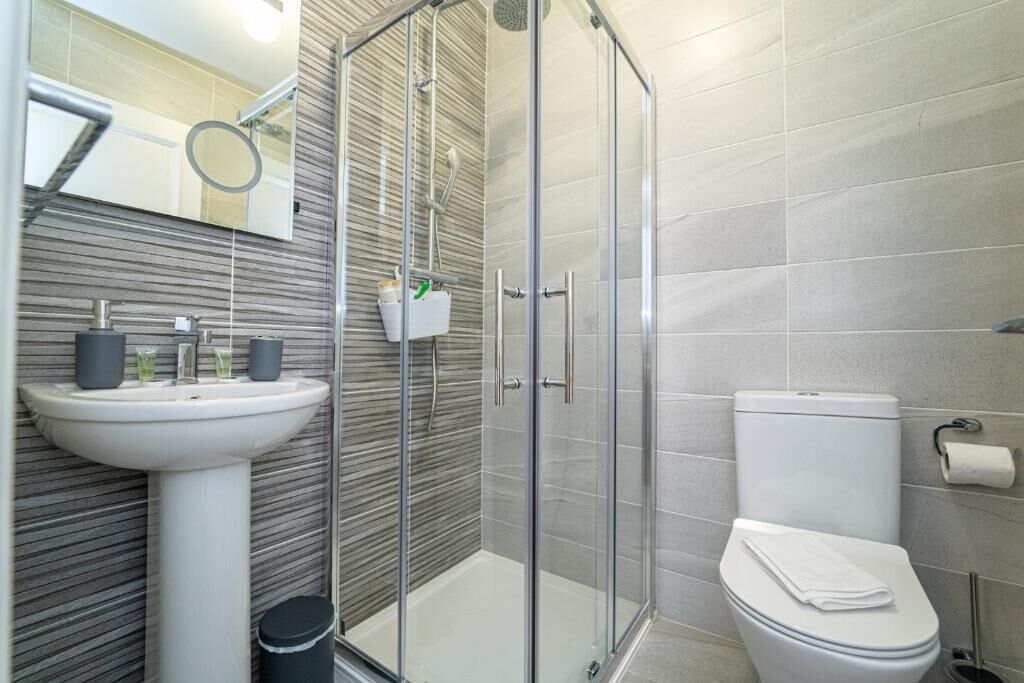 Un baño moderno con ducha de vidrio, lavamanos pedestal y retrete.