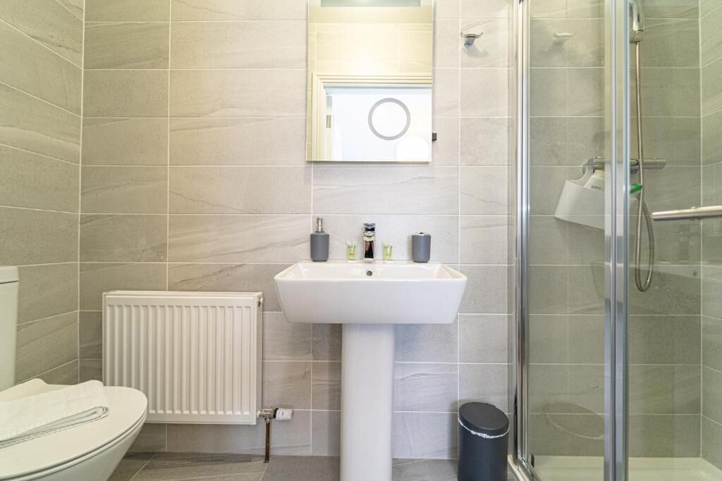 Un baño con lavabo blanco, inodoro, cabina de ducha con mampara de cristal y espejo sobre el lavabo.