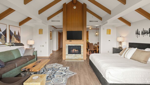 Habitació moderna amb llar de foc, llit, sofà i zona de menjador.