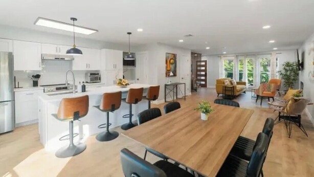 Una cocina moderna con armarios blancos, una isla central con taburetes y un comedor con mesa y sillas de madera.