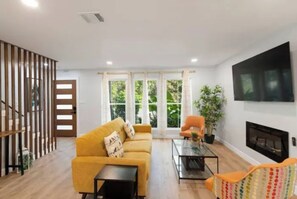 Ein Wohnzimmer mit einer Couch, Sesseln, Fernseher, Kamin und großen Fenstern.