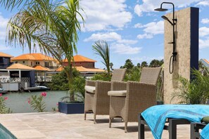 A poolside area with wicker chairs, a covered table, and a shower. - Blue Lagoon with a lovely private pool and views over the lagoon (Kralendijk)