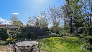 A patio with a round metal table and chairs, surrounded by a garden with various plants and a lawn. - Uphill Broadway (Lincoln)