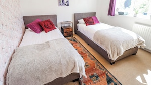 A bedroom with two beds, a nightstand, a painting, and a window with curtains. - Uphill Broadway (Lincoln)