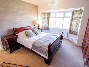 A bedroom with a wooden bed, a nightstand, a bedside table, a window with curtains, and a radiator. - Uphill Broadway (Lincoln)