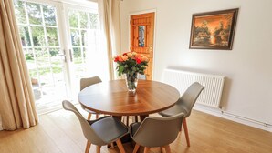 A dining area with a round wooden table, four chairs, a vase with flowers, a window with curtains, a radiator, and a framed picture on the wall. - Uphill Broadway (Lincoln)