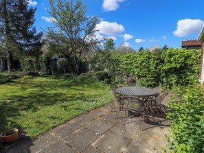 Eine Terrasse mit rundem Tisch und Stühlen, umgeben von einem Kiesweg und üppiger Bepflanzung.