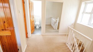 A hallway leading to a bathroom with a toilet, a mirror, and a wooden door. - Uphill Broadway (Lincoln)