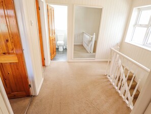 A hallway leading to a bathroom with a toilet, a mirror, and a wooden door. - Uphill Broadway (Lincoln)