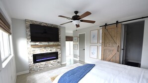Un dormitorio con chimenea, ventilador de techo, cama y una puerta corrediza de estilo granero.