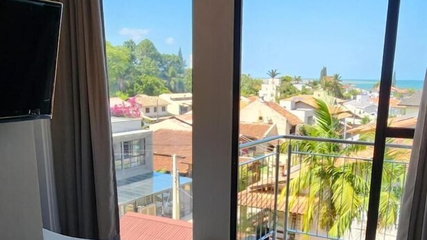 A hotel room with a large window, a bed, a small stool, and a TV. - Casa Arrô Pousada Boutique (Itajaí)