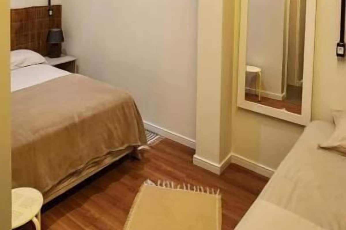 Ein Hotelzimmer mit Bett, Nachttisch, Lampe, Spiegel und einem kleinen Hocker.