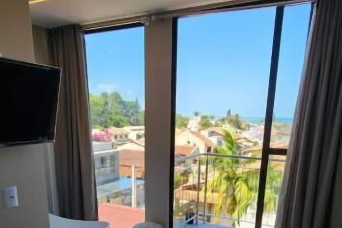 Ein Hotelzimmer mit Bett, Fernseher, Badewanne und Blick auf Stadt und Strand.