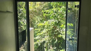 A window with a view of dense foliage and a white structure outside. - Casa Arrô Pousada Boutique (Itajaí)