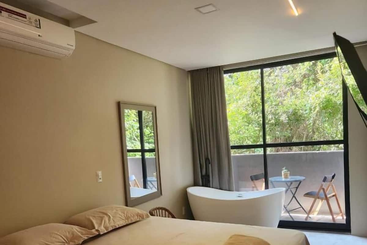 Ein Schlafzimmer mit Bett, Fenster, Spiegel und Blick ins Freie.