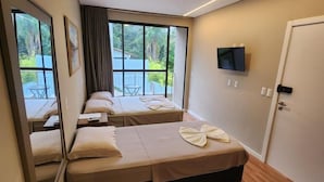 A hotel room with two beds, a TV, a door with a handle, and a window with a view of greenery. - Casa Arrô Pousada Boutique (Itajaí)