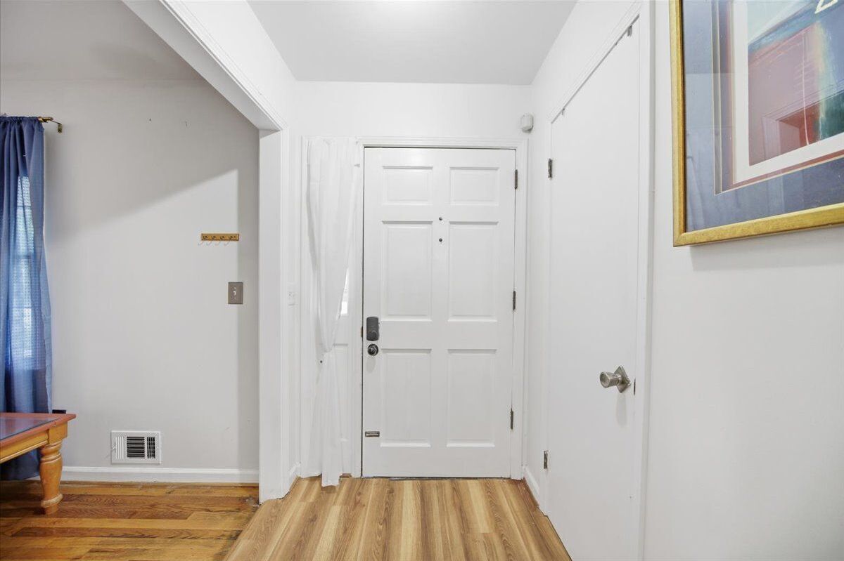 A hallway with a white door, a vent on the wall, and a framed picture on the right.
