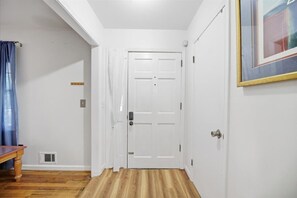 Ein Flur mit einer weißen Tür, einem Lüftungsgitter an der Wand und einem gerahmten Bild rechts.