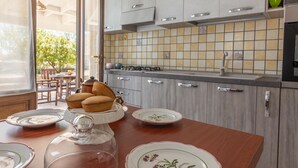 A kitchen with a tiled backsplash, wooden cabinets, and a dining table with plates and a glass dome. - Villa Miravalle - Salve (Salve)