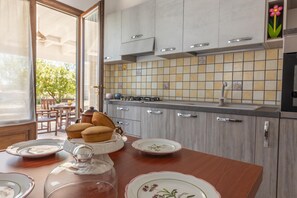 A kitchen with a tiled backsplash, wooden cabinets, and a dining table with plates and a glass dome. - Villa Miravalle - Salve (Salve)