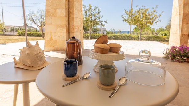 A table with a ceramic cup, a teapot, a sugar bowl, a glass dome, and a plate with pastries. - Villa Miravalle - Salve (Salve)