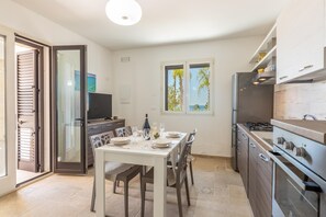 A modern kitchen with a dining area, a TV, and a view of palm trees through the window. - Villa Miravalle - Salve (Salve)