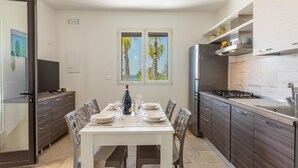 A modern kitchen with a dining table set for four, a built-in stove, and a large window with a view of palm trees. - Villa Miravalle - Salve (Salve)