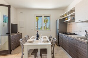 A modern kitchen with a dining table set for four, a built-in stove, and a large window with a view of palm trees. - Villa Miravalle - Salve (Salve)