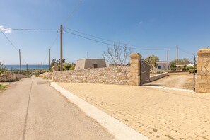 A paved road leading to a stone wall with a gate, a clear sky, and a distant view of the sea. - Villa Miravalle - Salve (Salve)