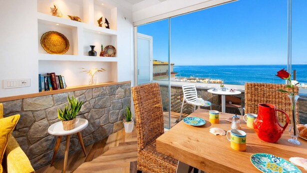 A modern room with a large window overlooking the sea, wicker furniture, and a stone wall. - AMORE RENTALS - Apartment Seapearl Sorrento with Sea View, Near the Beach (Sorrento)