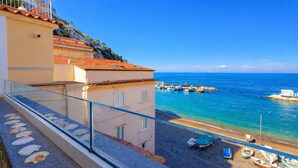 A coastal building with a balcony overlooking a beach with boats and a clear blue sky. - AMORE RENTALS - Apartment Seapearl Sorrento with Sea View, Near the Beach (Sorrento)