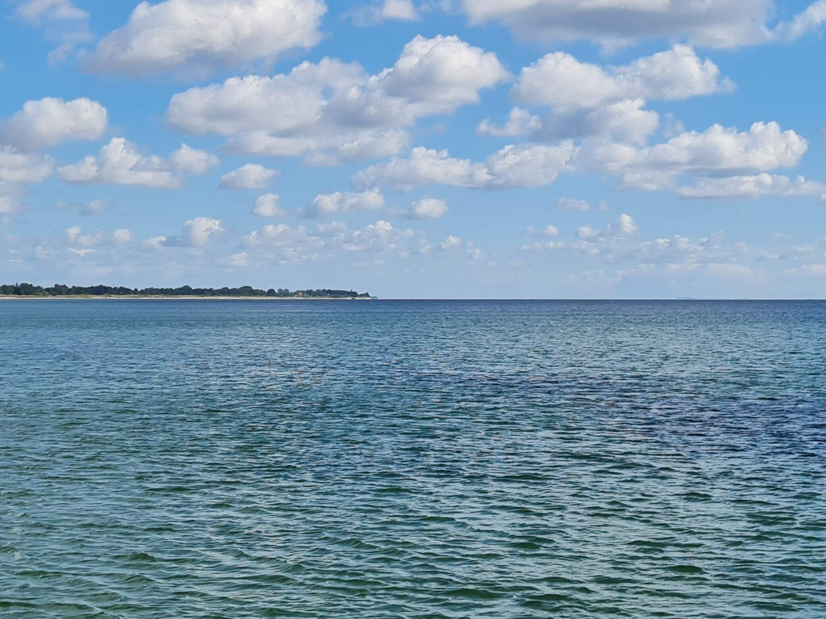 A calm sea with a distant shoreline and scattered clouds.