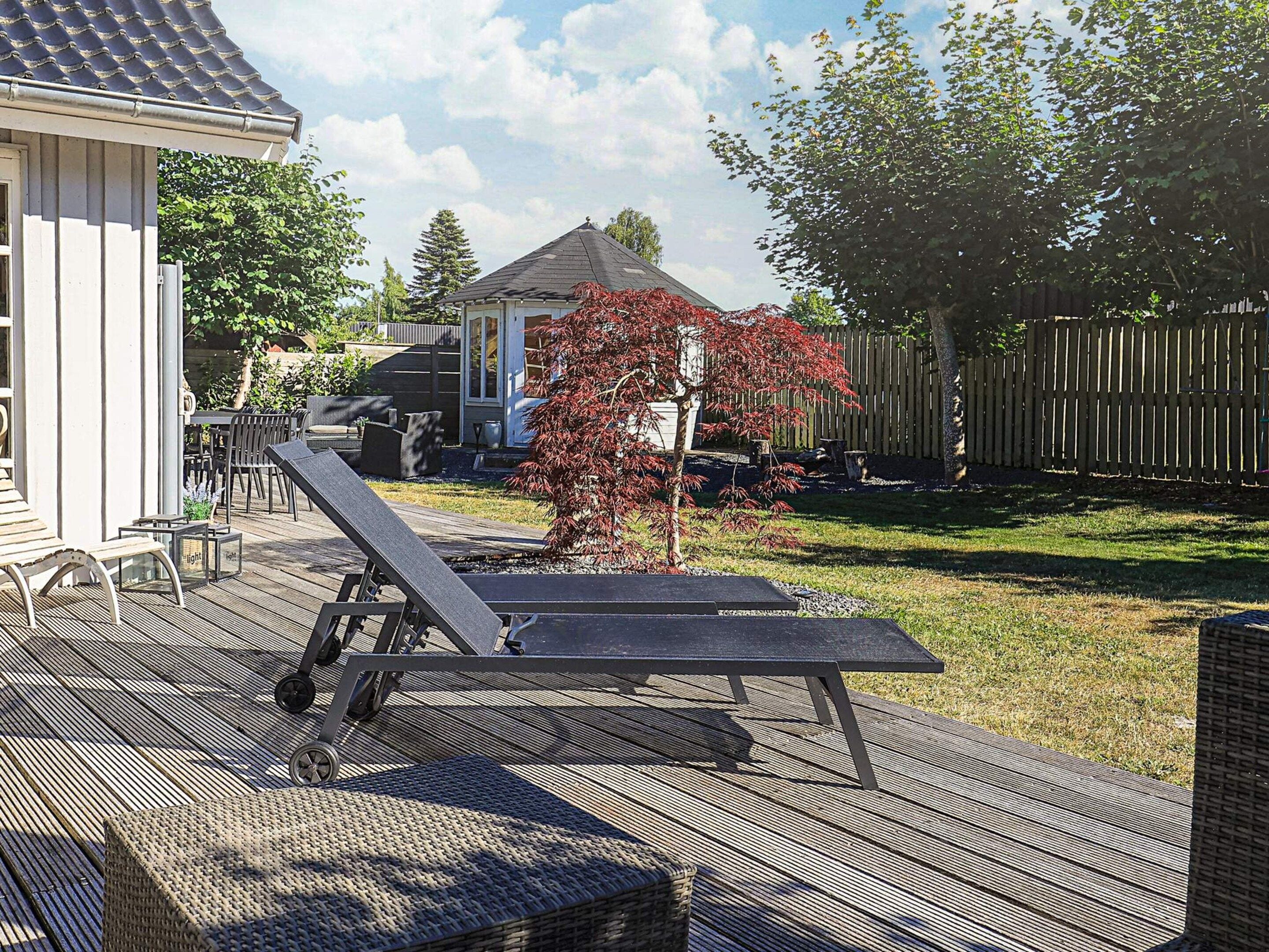 An outdoor deck with a sun lounger, a small table, and a wicker chair.