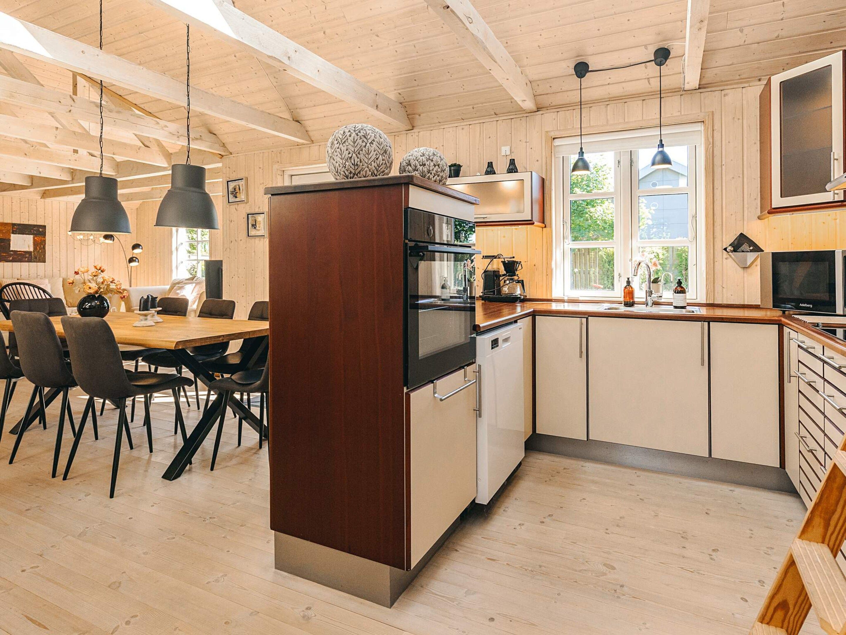 A modern kitchen with wooden cabinets, a dining area with chairs, and pendant lighting.