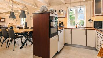A modern kitchen with wooden cabinets, a dining area with chairs, and pendant lighting.