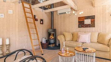 A cozy room with a wooden interior, a sofa, a ladder, a fireplace, and a hanging light fixture.
