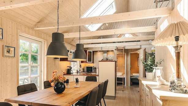 Una cocina amplia con armarios de madera, una isla central, iluminación colgante y vista a un dormitorio por una puerta abierta.