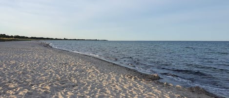 A sandy beach with gentle waves, a clear sky, and a distant shoreline.