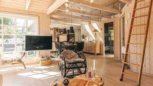 Un amplio salón con piso de madera, una mesa redonda de madera, un televisor y un comedor con sillas.