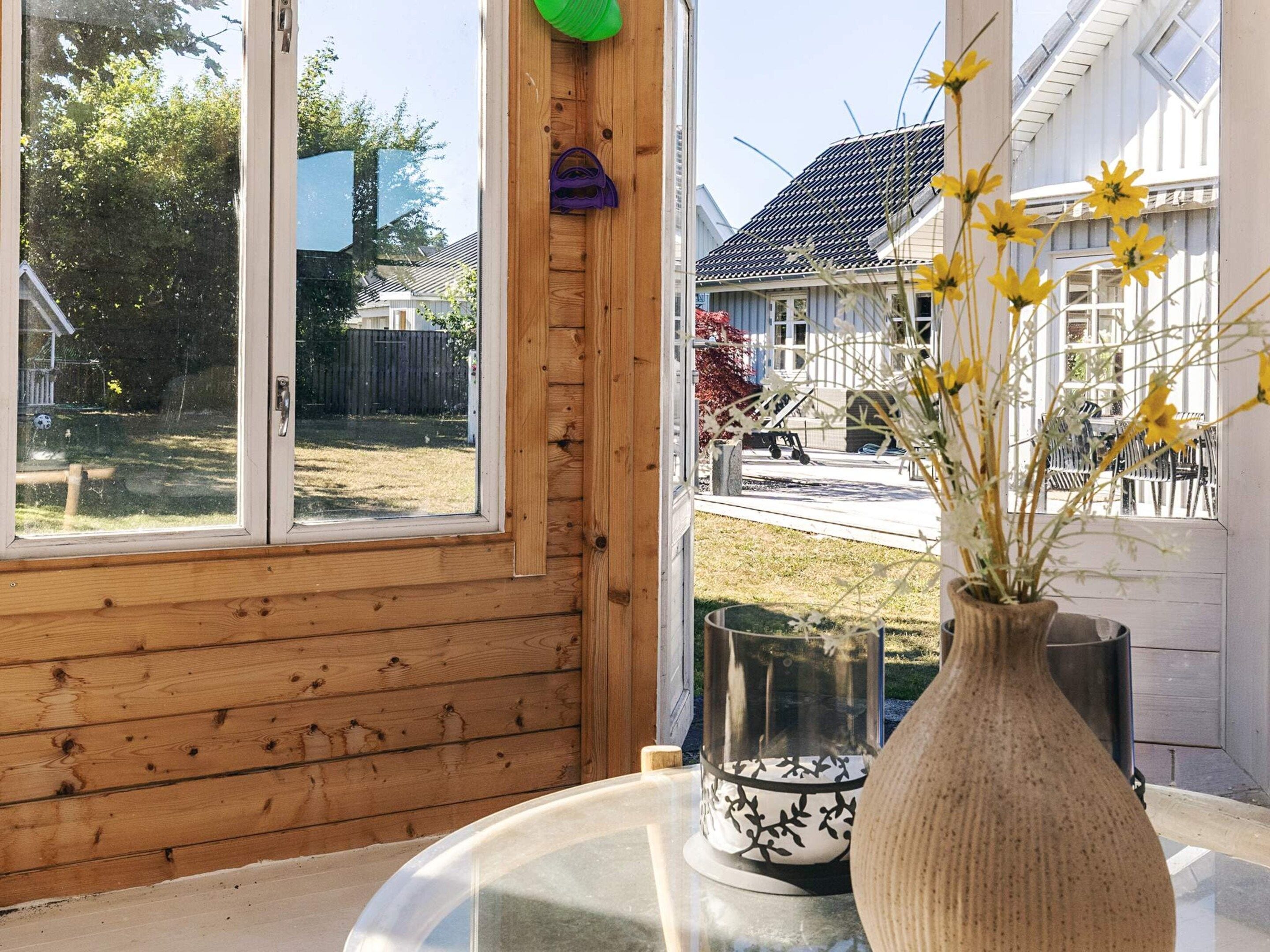 Una stanza con un'ampia finestra, una parete in legno, un tavolo con un vaso di fiori e un oggetto decorativo appeso al muro.