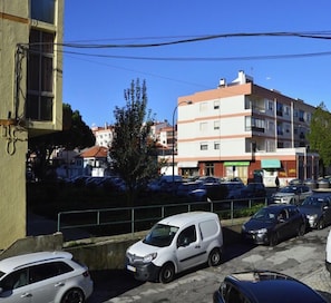 Ein Parkplatz mit mehreren Autos, einem weißen Lieferwagen und einem mehrstöckigen Gebäude mit Balkonen im Hintergrund.