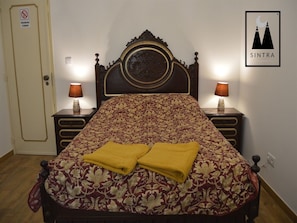 Ein Bett mit floralem Überwurf, zwei Nachttischlampen und ein an der Wand befestigtes Schild.
