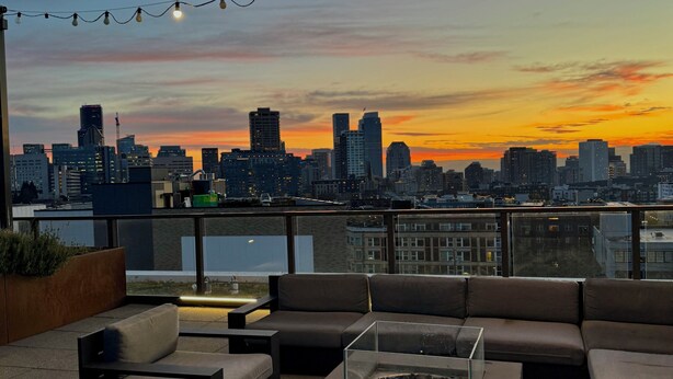 A rooftop terrace with outdoor seating, a view of the city skyline, and string lights. - Cozy 1-bedroom apartment with AC in vibrant Seattle neighborhood (Seattle)