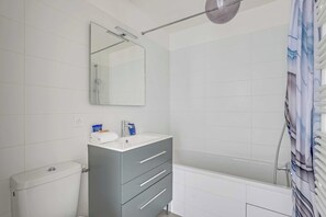 A bathroom with a toilet, a sink with a mirror, and a bathtub. - Cosy Flat - 1bdr/4p - View on the Sacre-coeur (Paris)