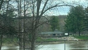A lake with a dock, a building in the background, and a dirt road in the foreground.