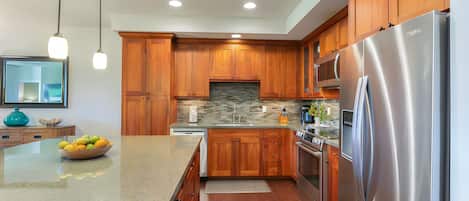 A modern kitchen with wooden cabinets, a stainless steel refrigerator, and a granite countertop.