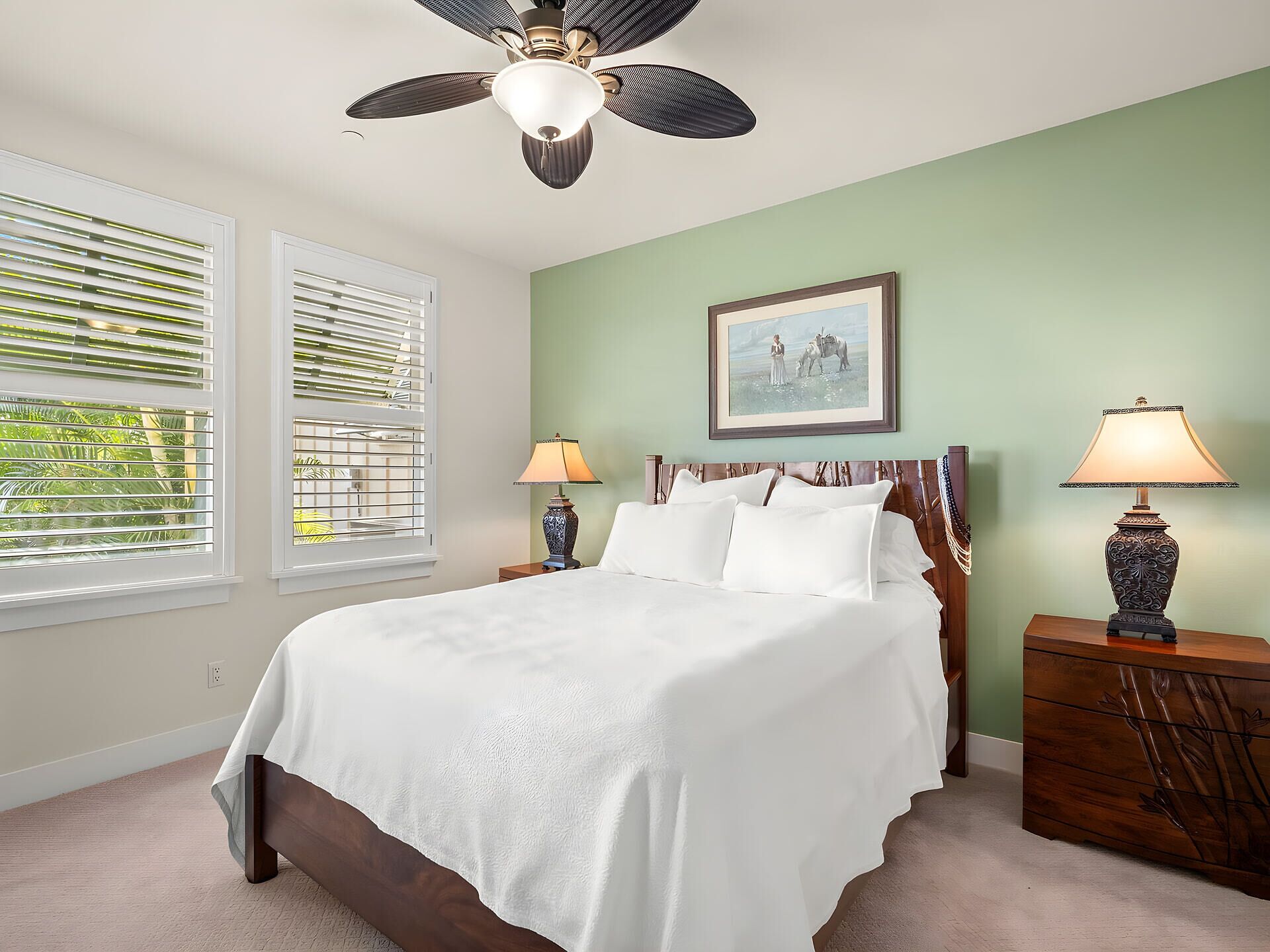 A bedroom with a bed, two bedside lamps, a ceiling fan, and a framed picture on the wall.